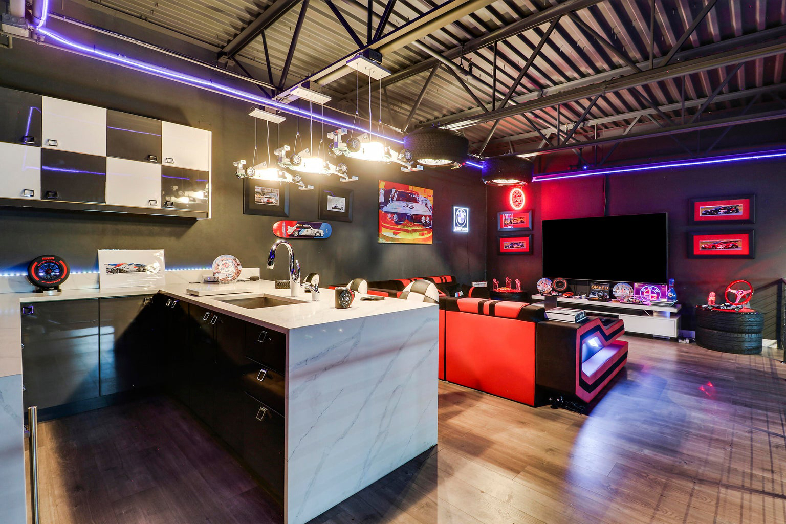 Modern entertainment room with a black and white kitchen island, red and black seating, racing-themed decor, and overhead car wheel lights.