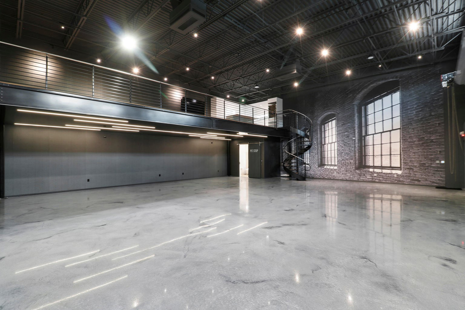 Spacious modern industrial loft with polished concrete floor, black metal spiral staircase, mezzanine level, and large mural.