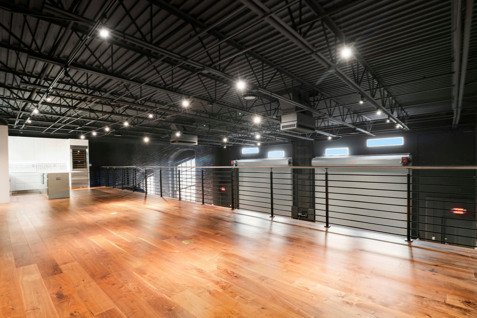 Modern loft-style interior with wooden floor, black metal railing, and exposed industrial ceiling with spotlights.