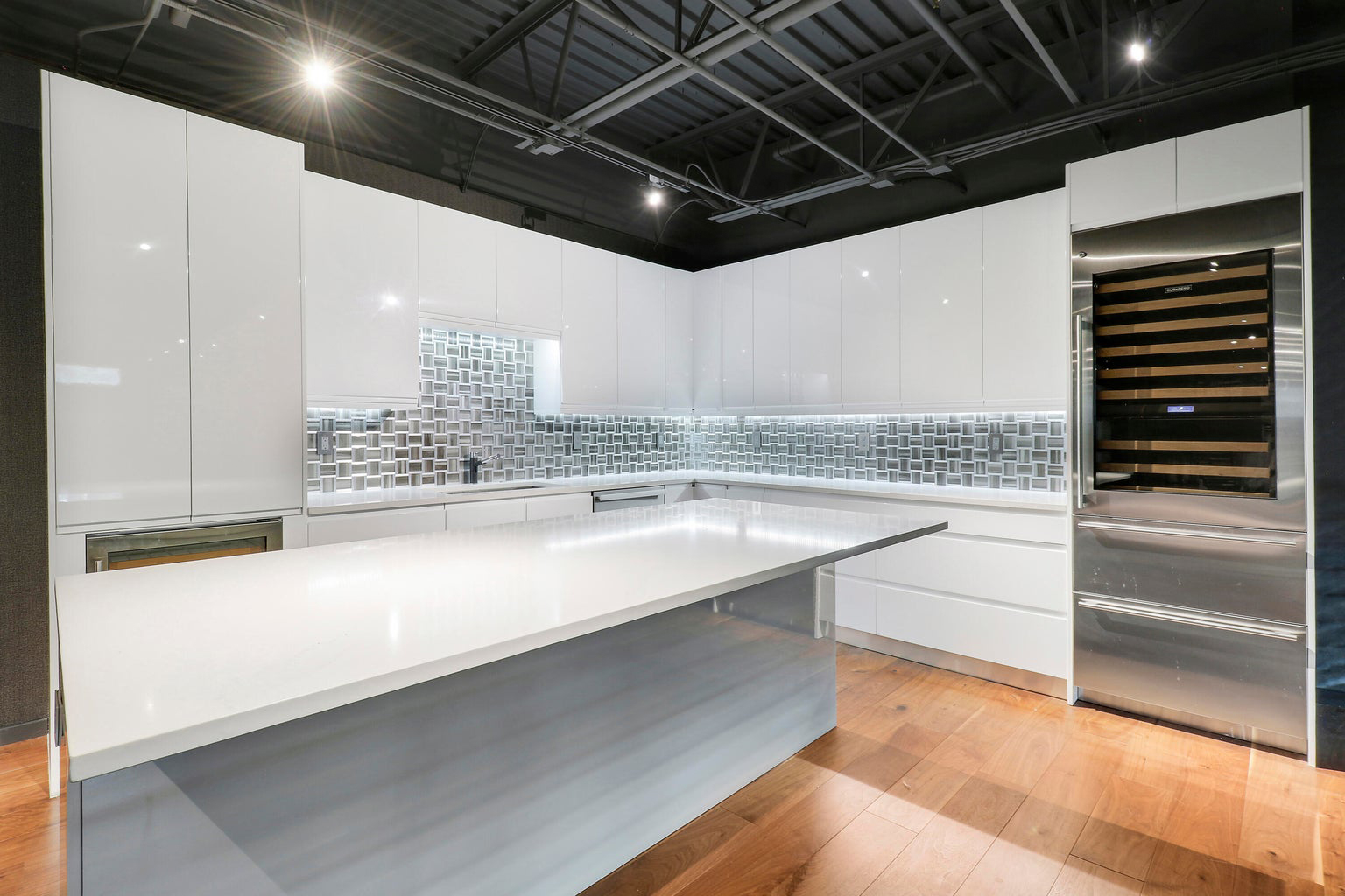 Modern kitchen with white high-gloss cabinets, geometric tile backsplash, and large white island countertop.