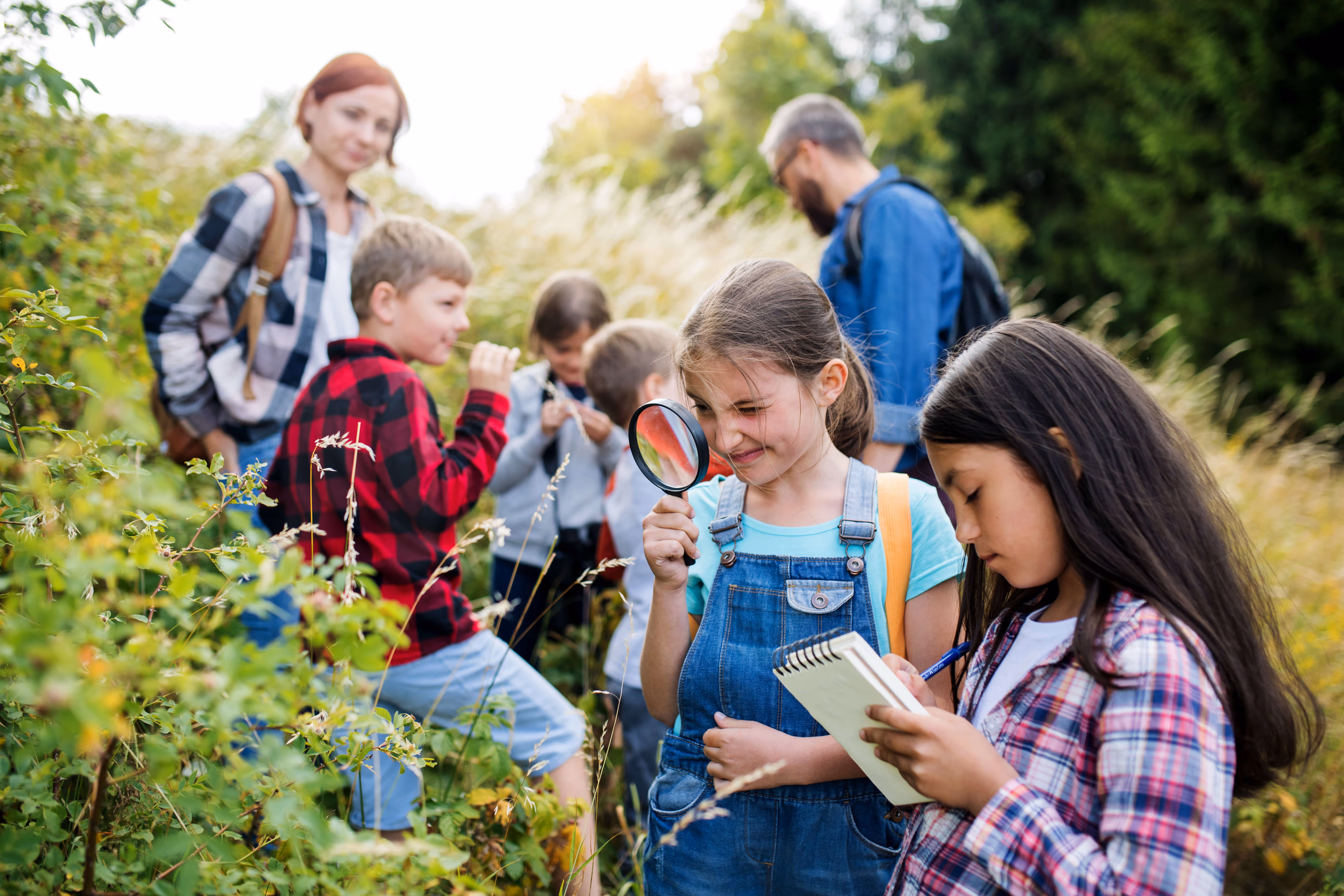 kids studying plants outside with magnifying glass and notepad