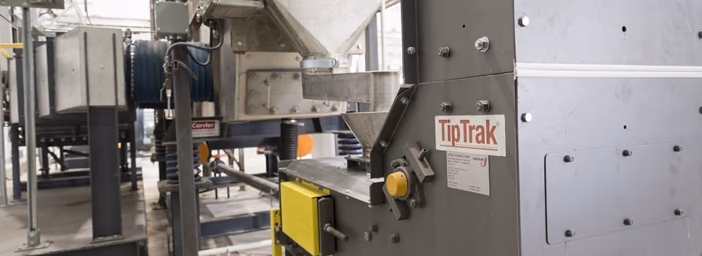 Industrial TipTrak machinery with metal components and yellow control box in a factory setting.