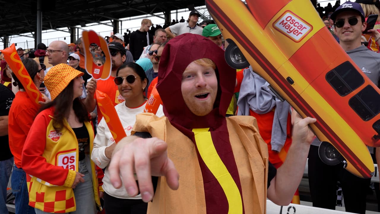 A Wienie 500 fan in a hot dog costume with a Wienermobile sign