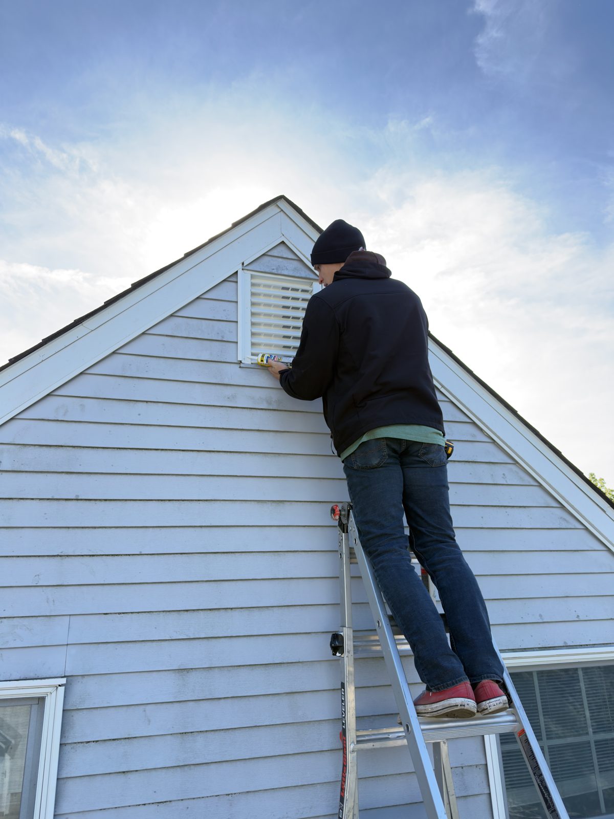 Crew member repairing an attic vent on a ladder
