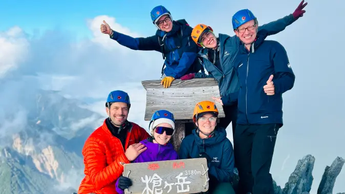 Groupe de six alpinistes souriants posant au sommet d’une montagne.