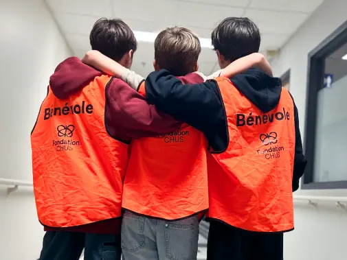 Trois jeunes bénévoles en gilet orange de la Fondation CHUS, bras dessus-dessous.