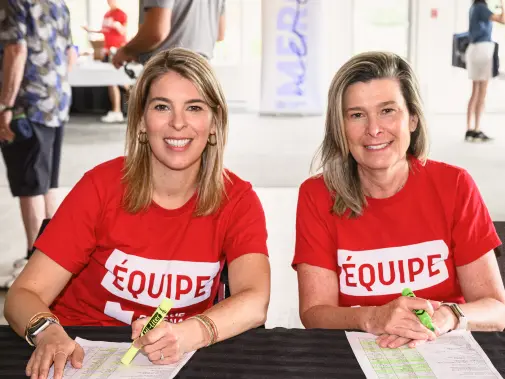 Deux bénévoles en t-shirt rouge “Équipe” souriant à une table d’inscription.