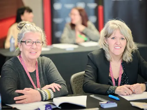 Deux femmes assises derrière une table d’accueil avec documents.