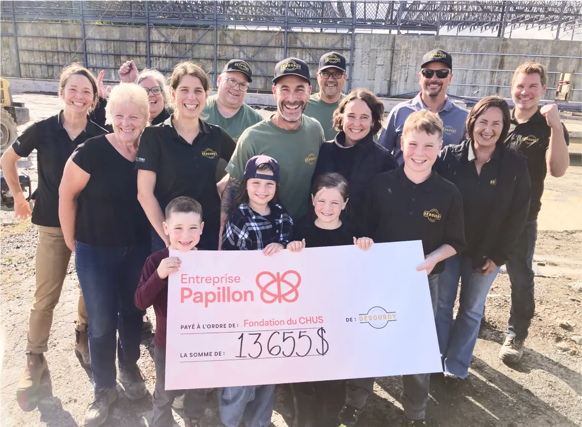 Un groupe de familles et employés de l’entreprise Excavation Desourdy sourient en extérieur et présentent un chèque de 13 655 $ remis à la Fondation du CHUS.