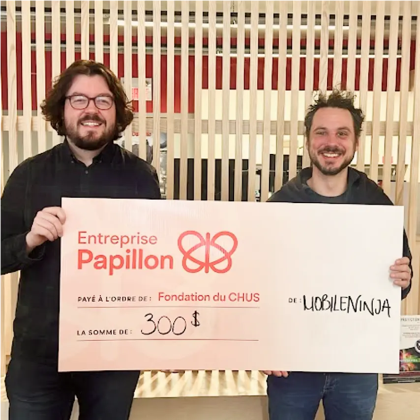 Deux jeunes hommes souriants tiennent un chèque de 300 $ remis à la Fondation du CHUS par l’entreprise EMobile Ninja, devant un décor moderne en bois.