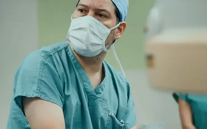 Chirurgien portant masque et tenue stérile en pleine intervention médicale.
