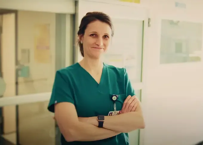 Infirmière en uniforme vert souriant bras croisés dans une unité hospitalière.