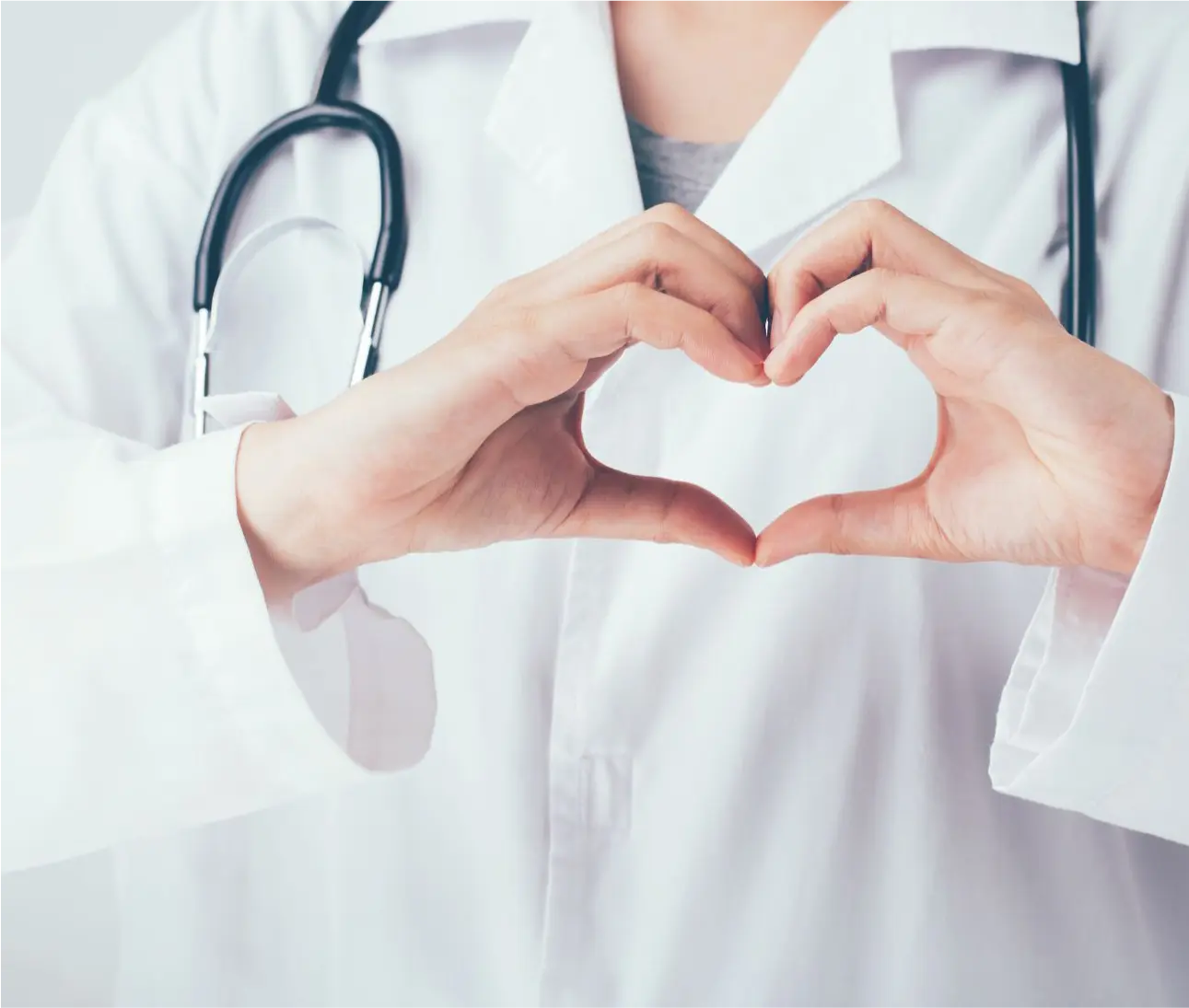 A doctor in a white coat with a stethoscope forms a heart with his hands in front of his chest.