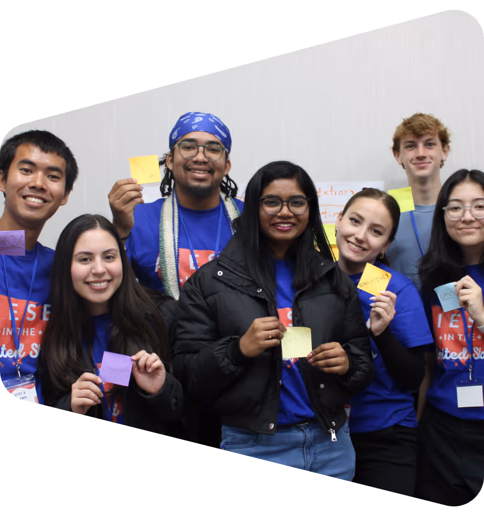 A group of diverse AIESEC US members smiling and holding colorful sticky notes with positive words during a leadership event, representing collaboration and empowerment among young leaders.