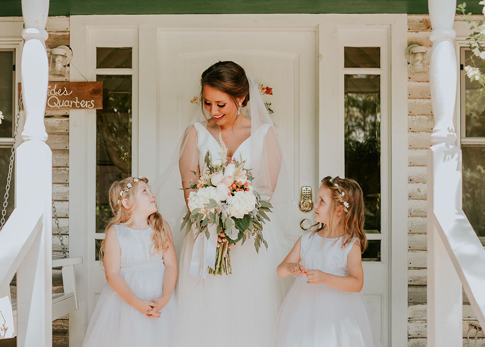 Bride poses with flower girls on the front porch of the Bridal Cottage at The Barn at Cedar Grove