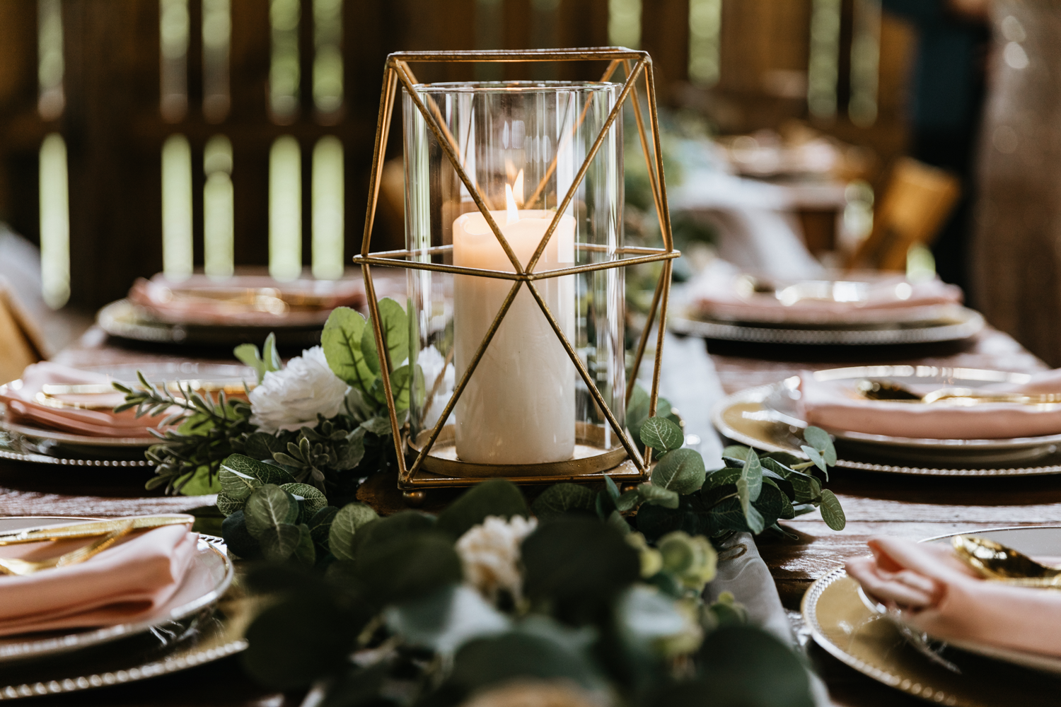 Wedding tablescape at The Barn at Cedar Grove shows table set with greenery and gold geometric candle holder as the centerpiece.  