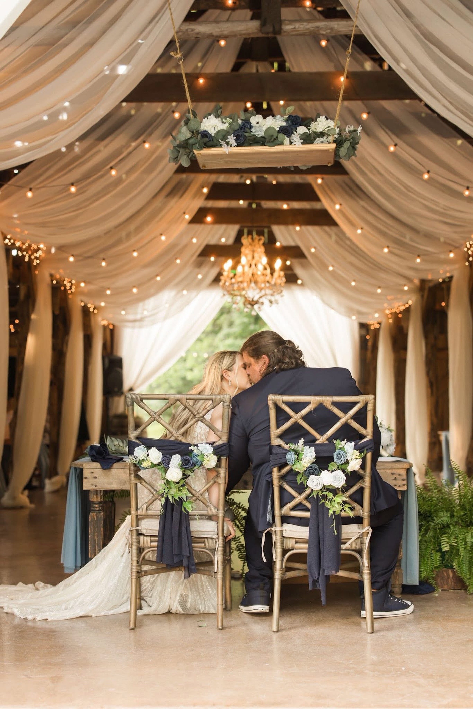 Couple enjoys a kiss while seated at the table during the wedding reception at The Barn at Cedar Grove