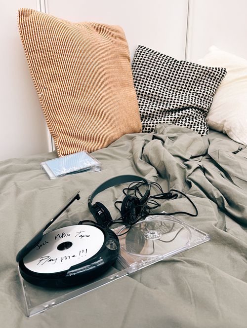 A section of a bed with soft furnishings, a CD Disman with headphones and a homemade mix CD inside it