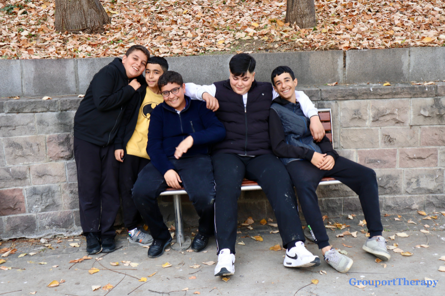 Teen boys sitting together on a park bench, representing adolescent friendship, peer support, and group therapy connection