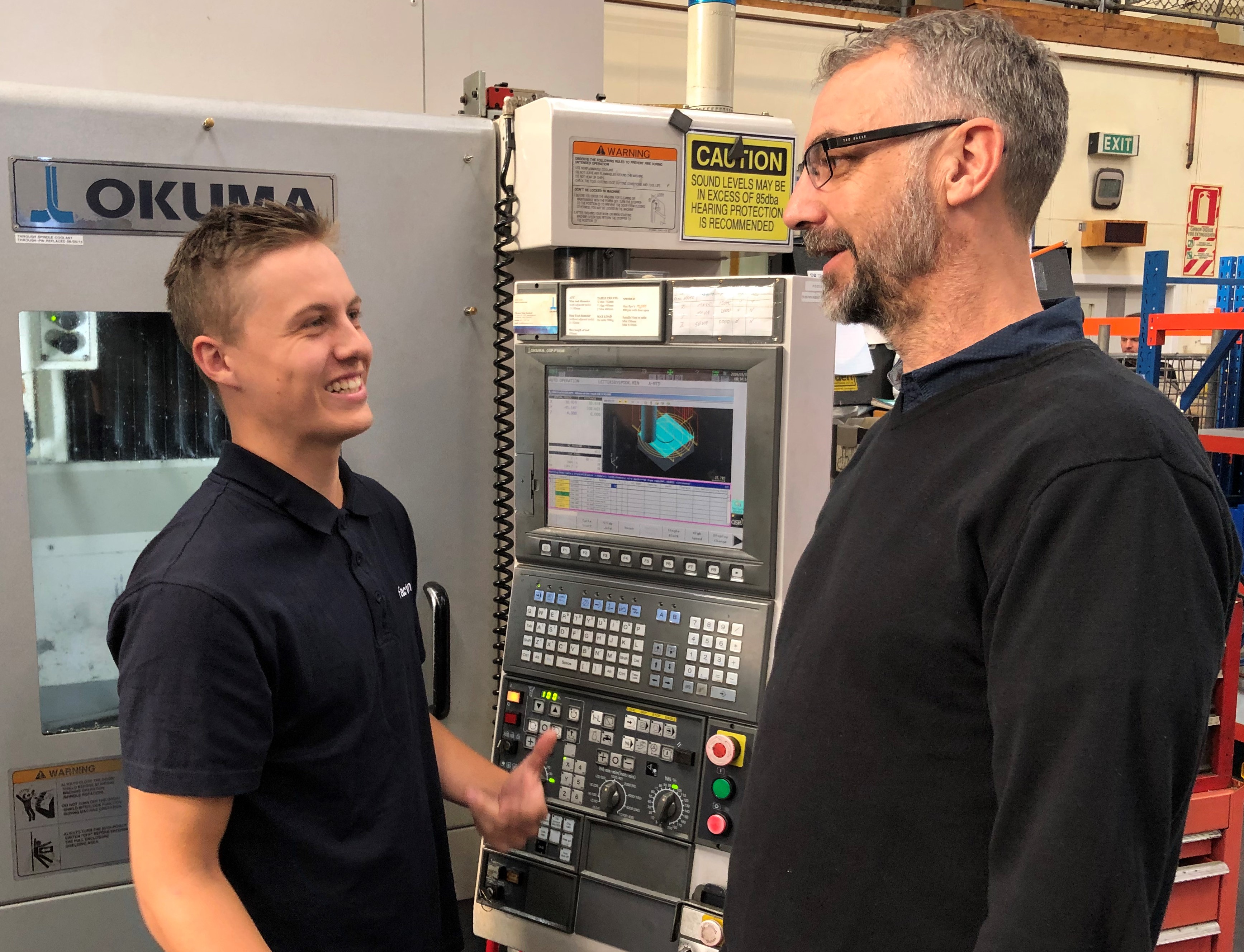 An apprentice talking with their workplace mentor beside industrial equipment