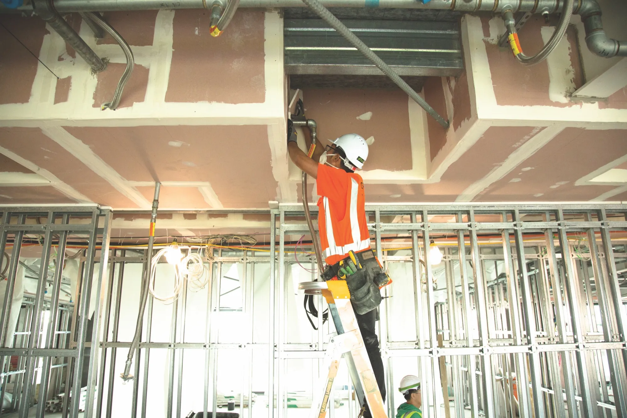 A coach observes an apprentice installing ceiling components