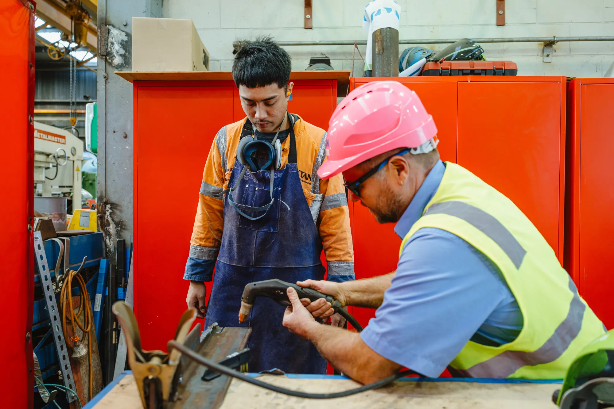A coach observes as an apprentice welds