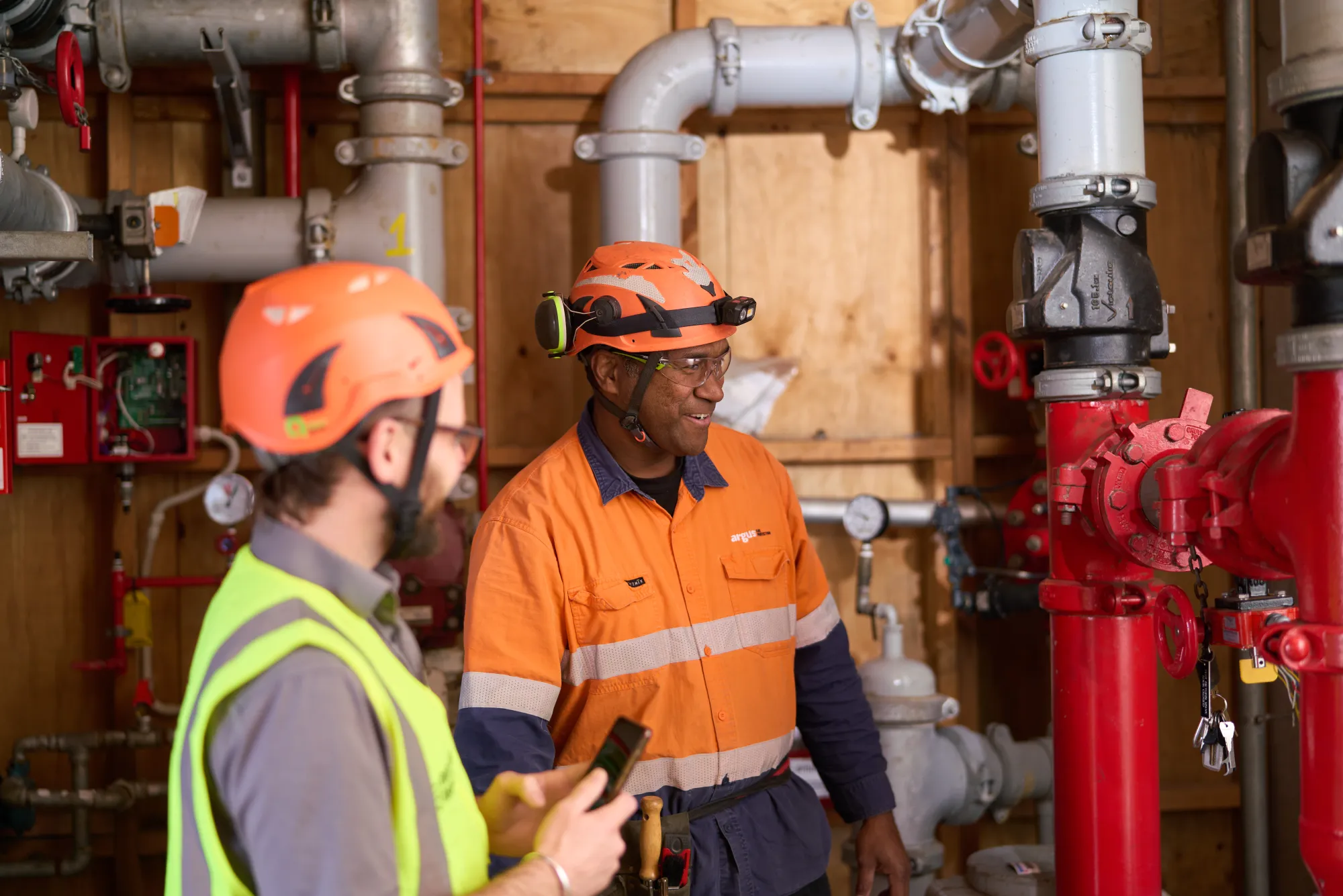 Two workers discussing equipment in a fire-systems mechanical room