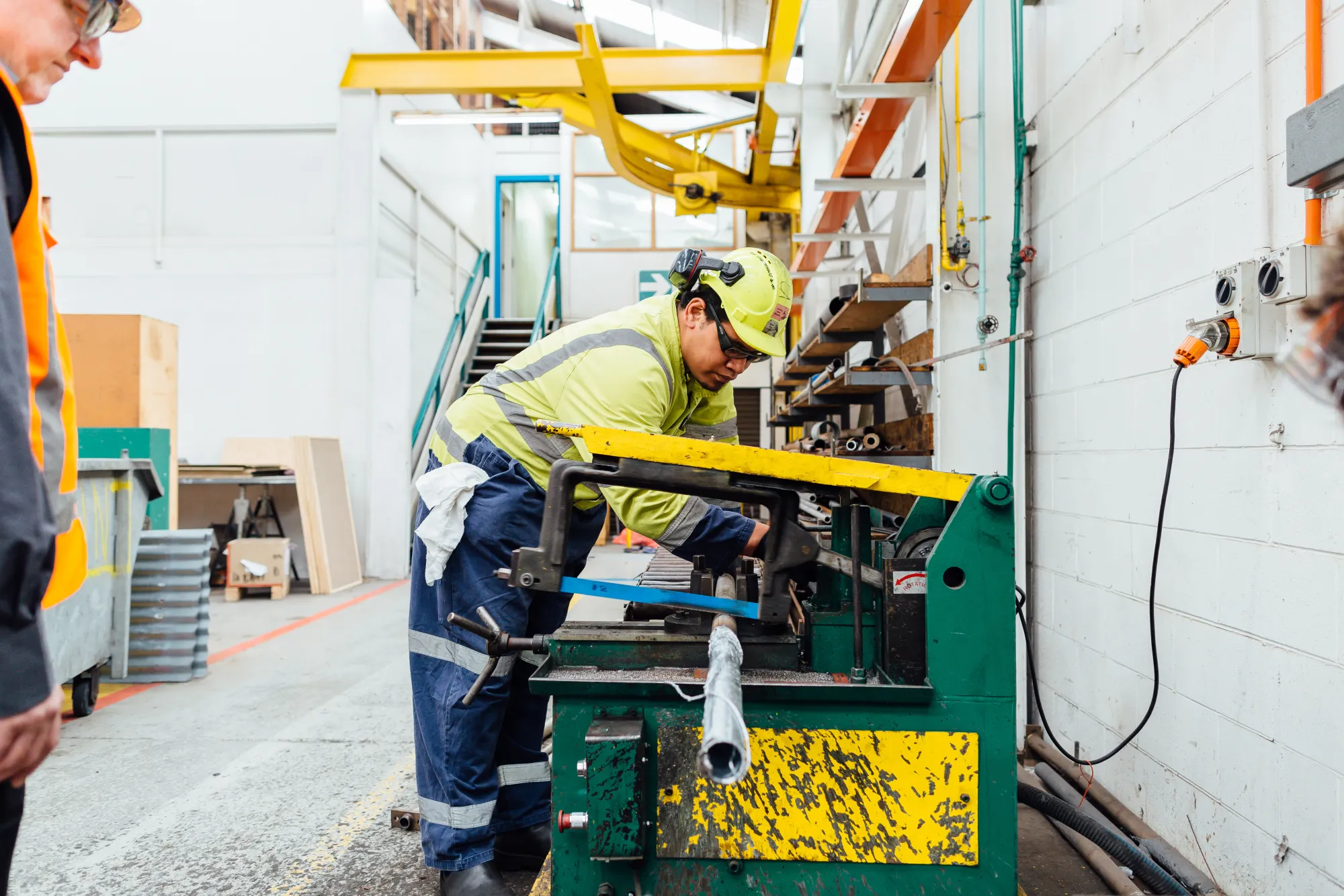 A coach guides an apprentice operating a pipe-bending machine
