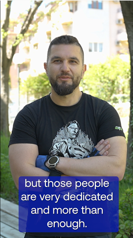 A person with a beard and a black shirt with a blue sign and a treeAI-generated content may be incorrect.