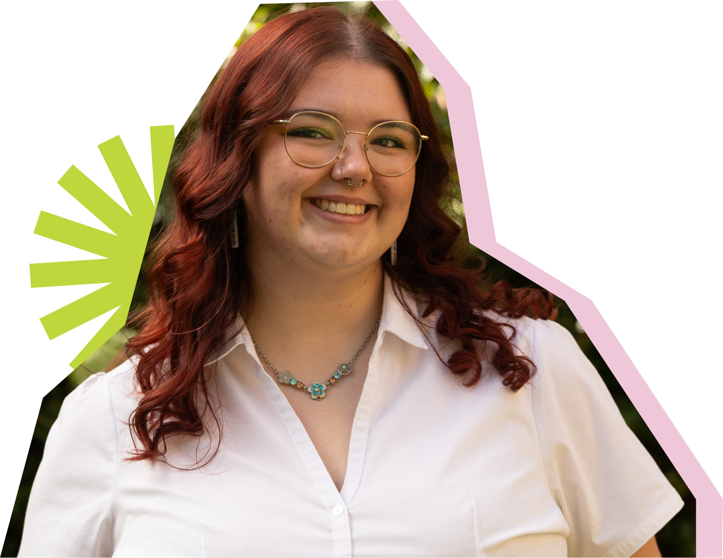 A female student outdoors smiling at the camera with a white shirt, red hair, glasses and a green pendent necklace. 