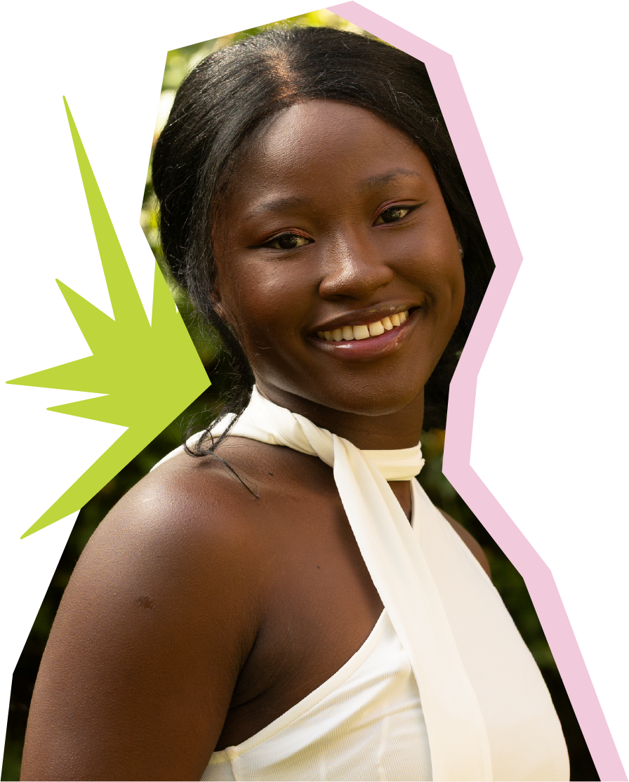 A female student outdoors smiling at the camera with a white shirt, red hair, glasses and a green pendent necklace.