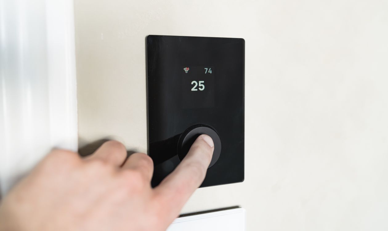 Main réglant un thermostat moderne pour piloter le chauffage d’un logement