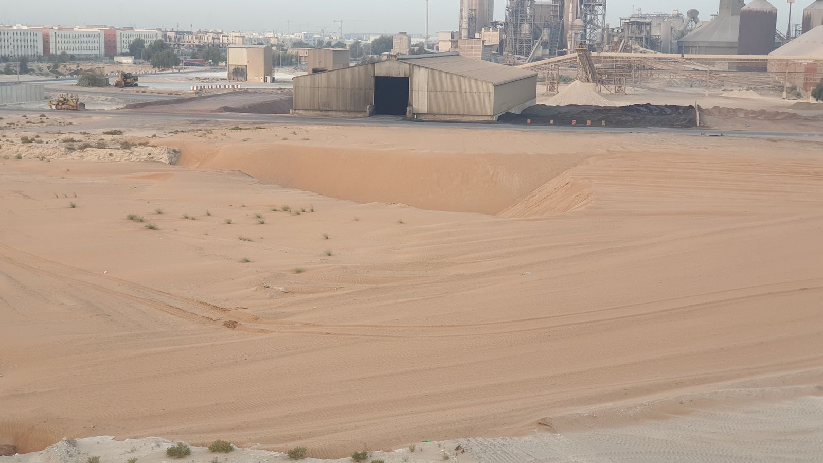 Terrain remué à proximité de bâtiments industriels dans un paysage dégagé