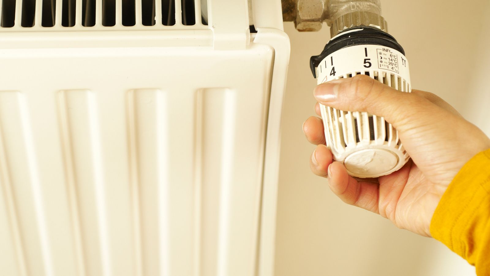 Main réglant le robinet thermostatique d’un radiateur blanc dans un logement