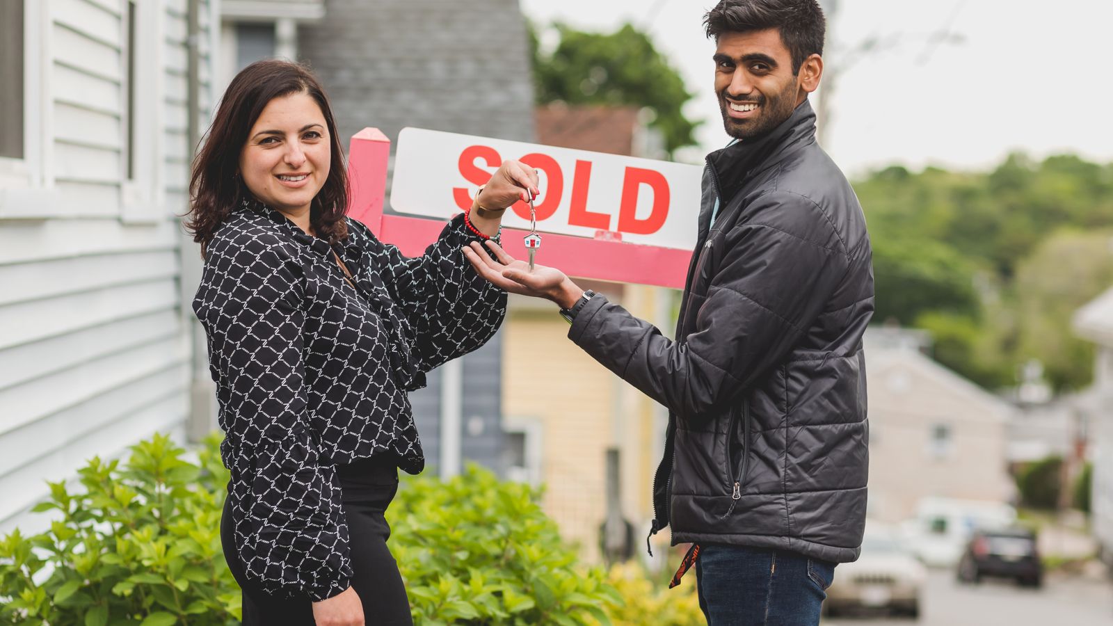 Couple recevant les clés d’un logement devant un panneau de vente