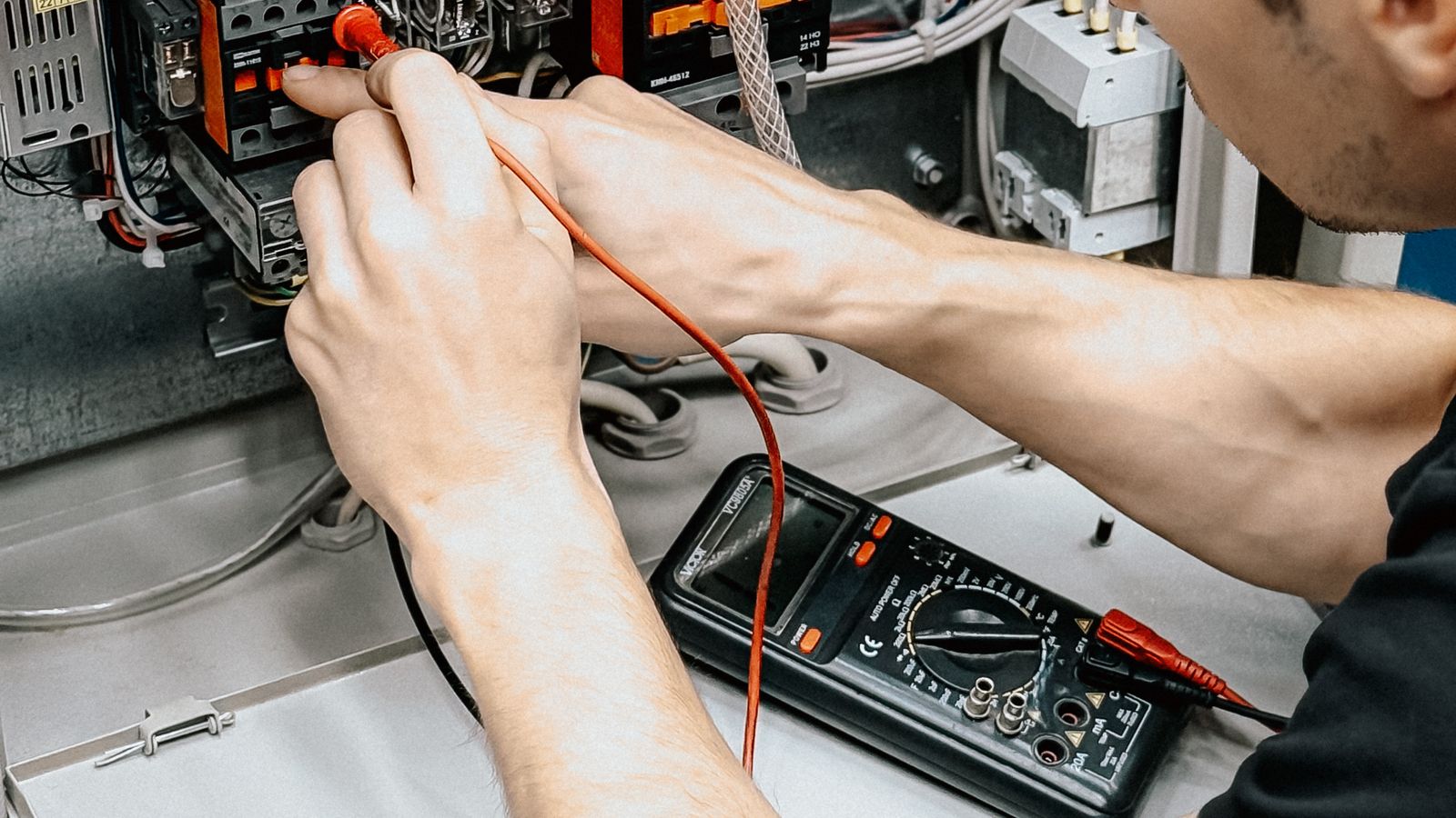 Électricien contrôlant un tableau électrique ouvert avec un appareil de mesure