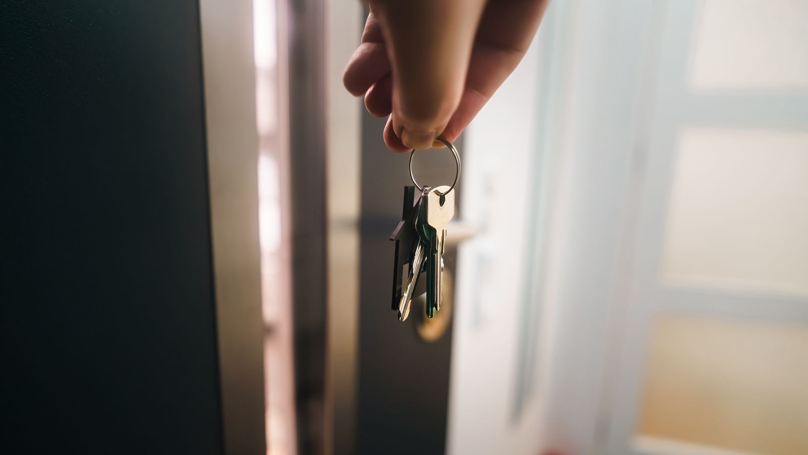 Main tenant les clés d’un logement devant une porte d’entrée