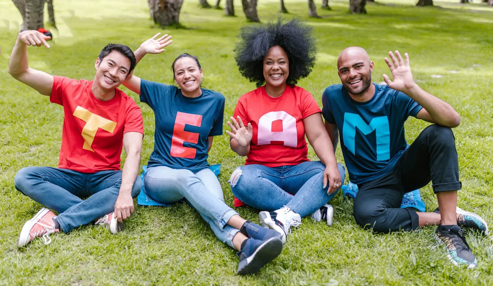 Four teachers sitting on the grass each with a letter on their t-shirts that make up the word: TEAM