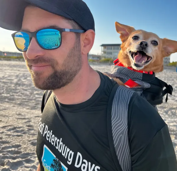 Fetch employee Bill T. walking on the beach with his dog in a backpack.
