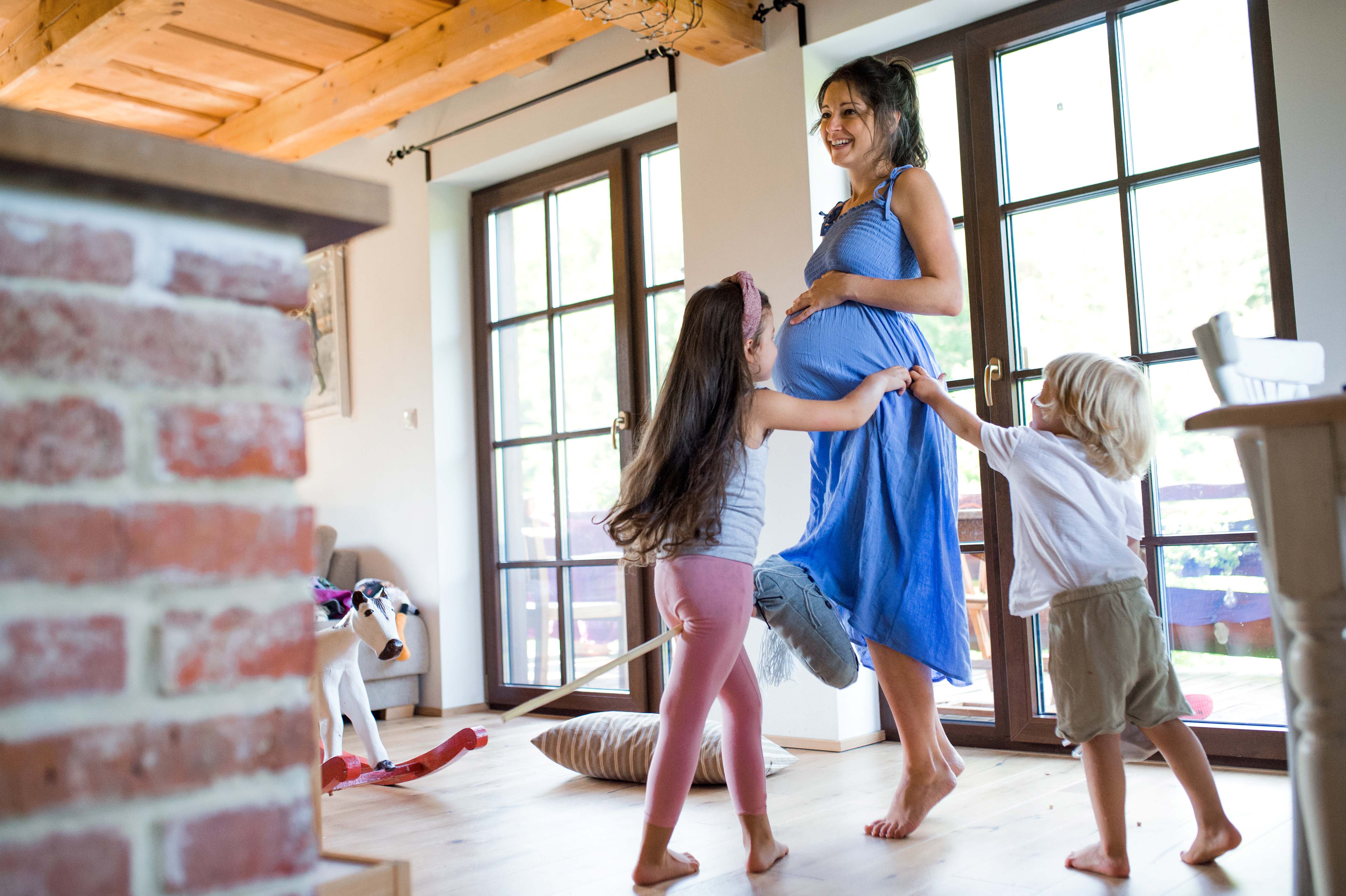 A pregnant mother smiling, her two kids touching her and laughing.