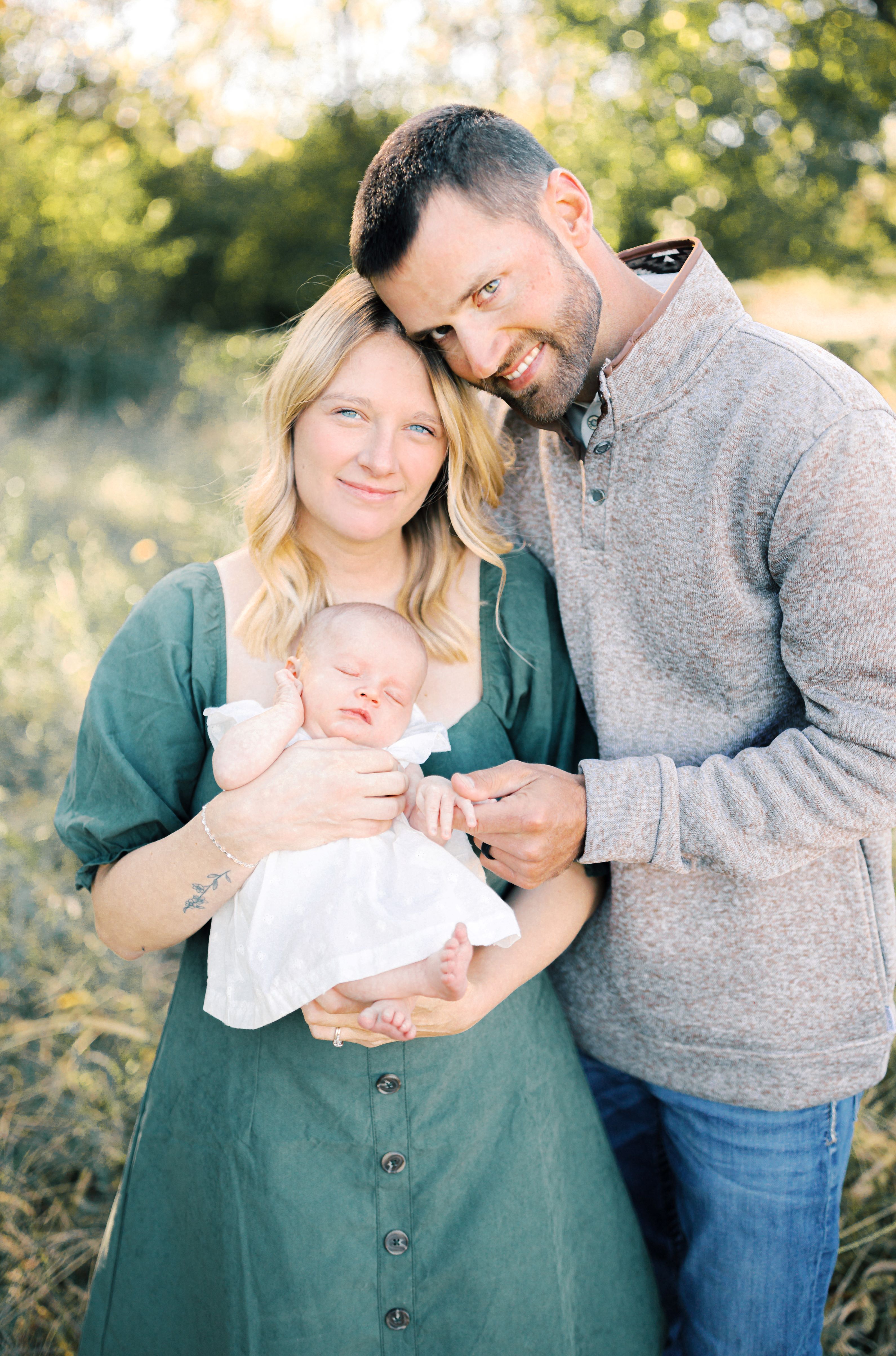 A woman holding a baby while a man is hugging the woman.