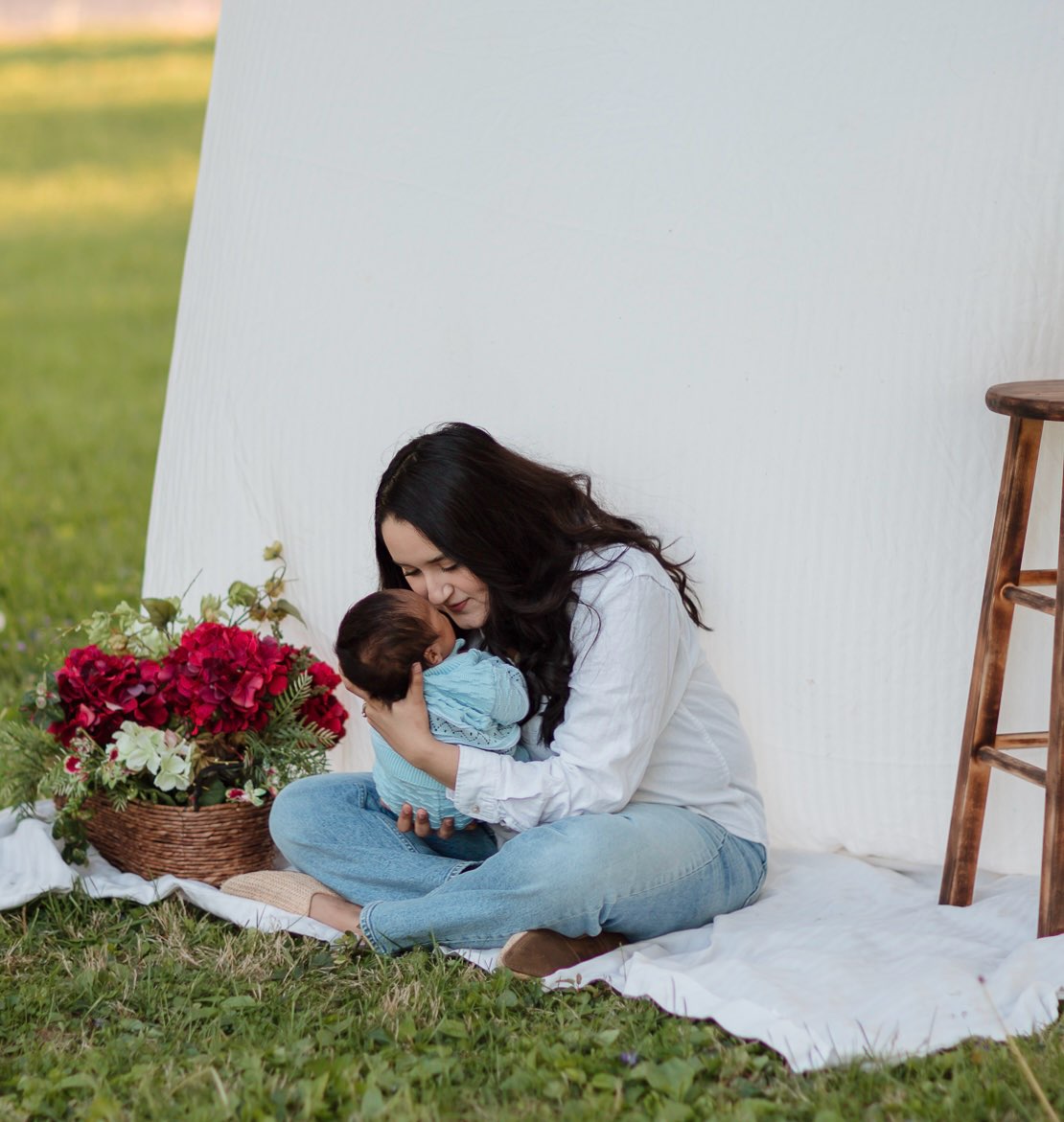 A mother holding her baby next to a basket of flowers.
