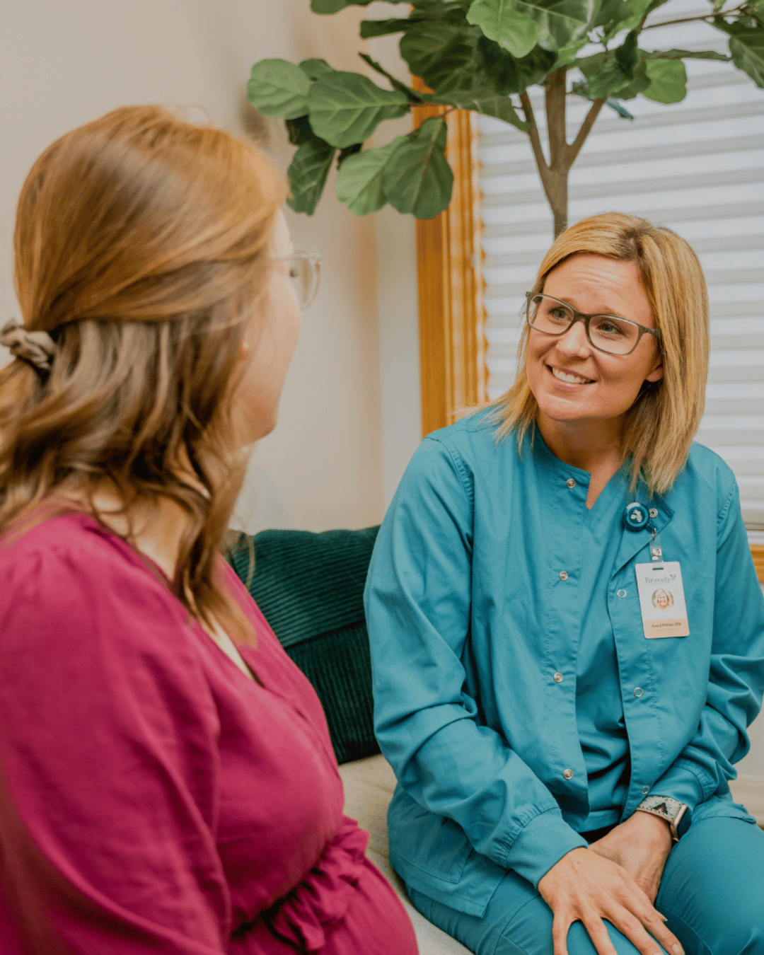 Pregnant woman talking with a smiling female healthcare professional wearing teal scrubs.