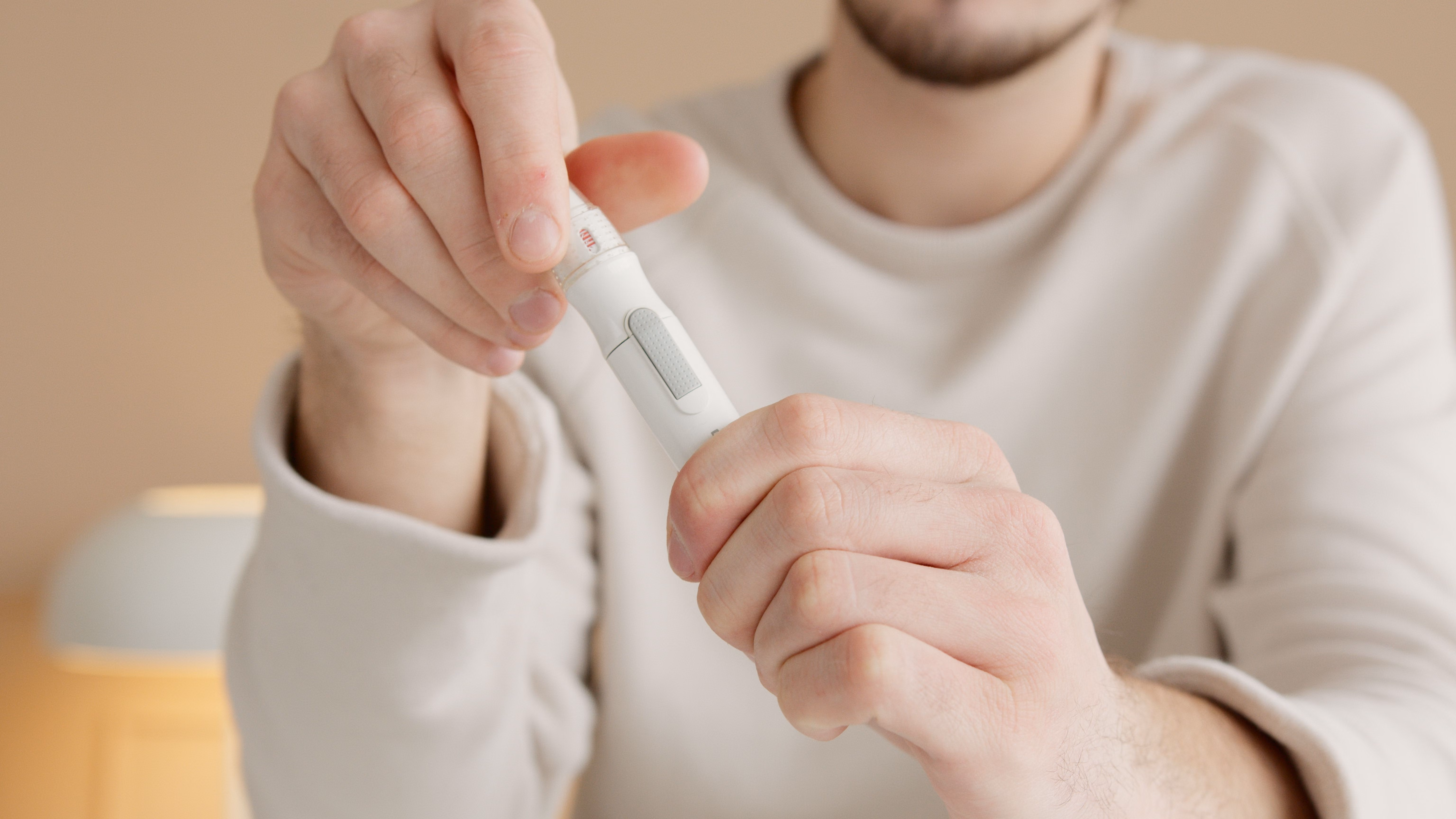 Close-up of a person holding a white lancing device, preparing to perform a blood glucose test.