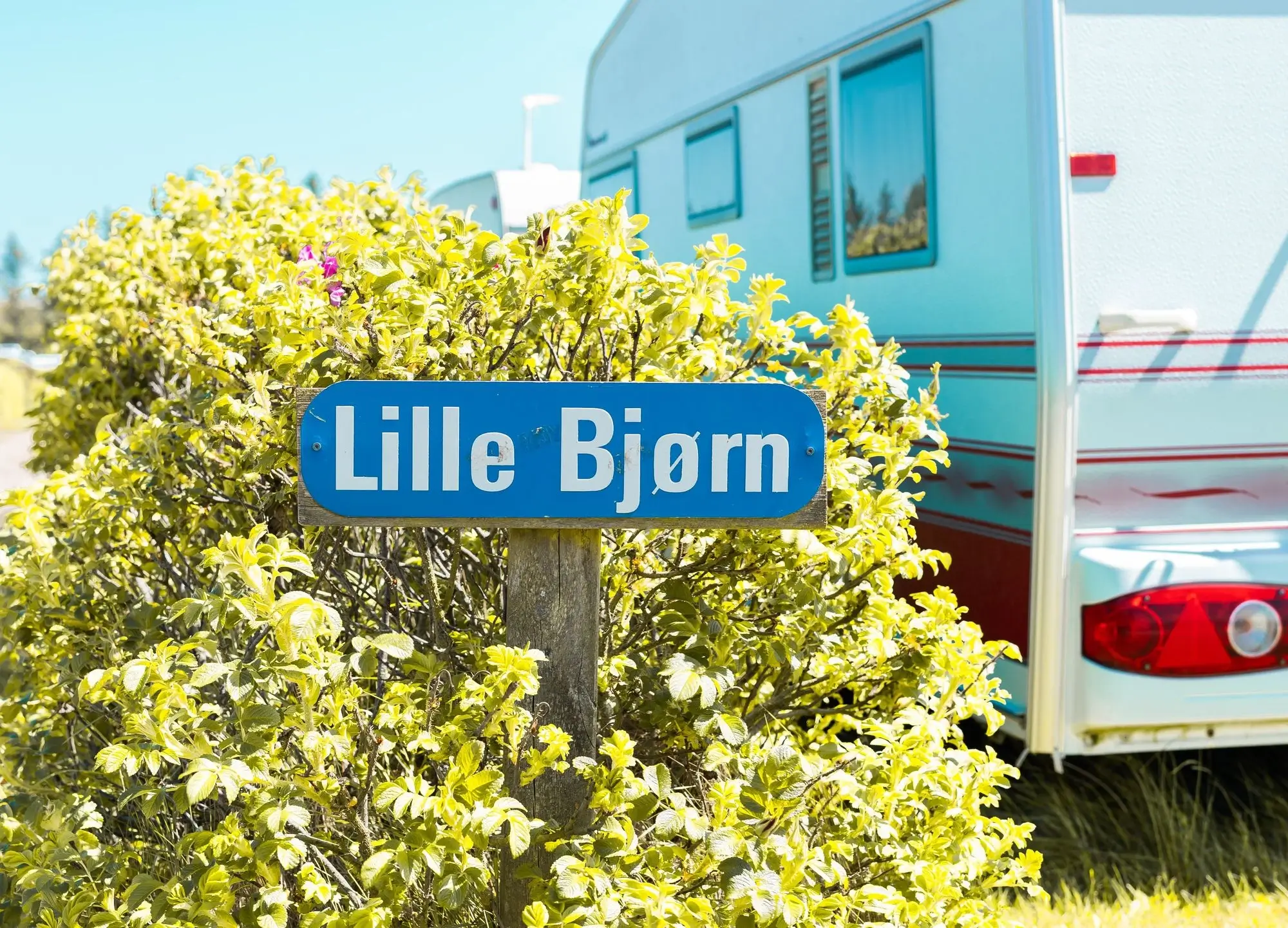 Vejskilt med "Lille Bjørn" på ved siden af en campingvogn