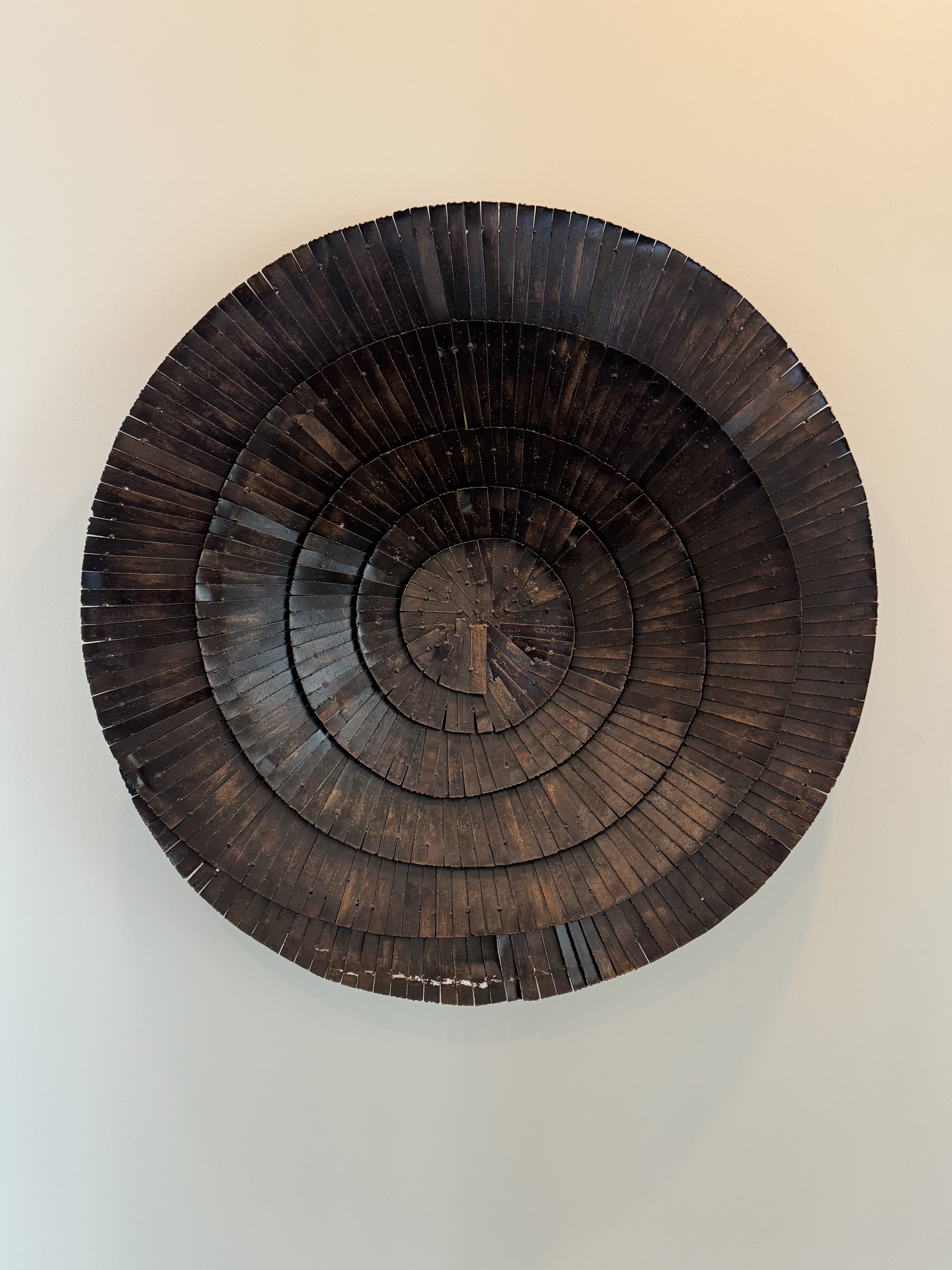 Wall-mounted circular wooden art piece with layered concentric rings of dark rectangular segments.