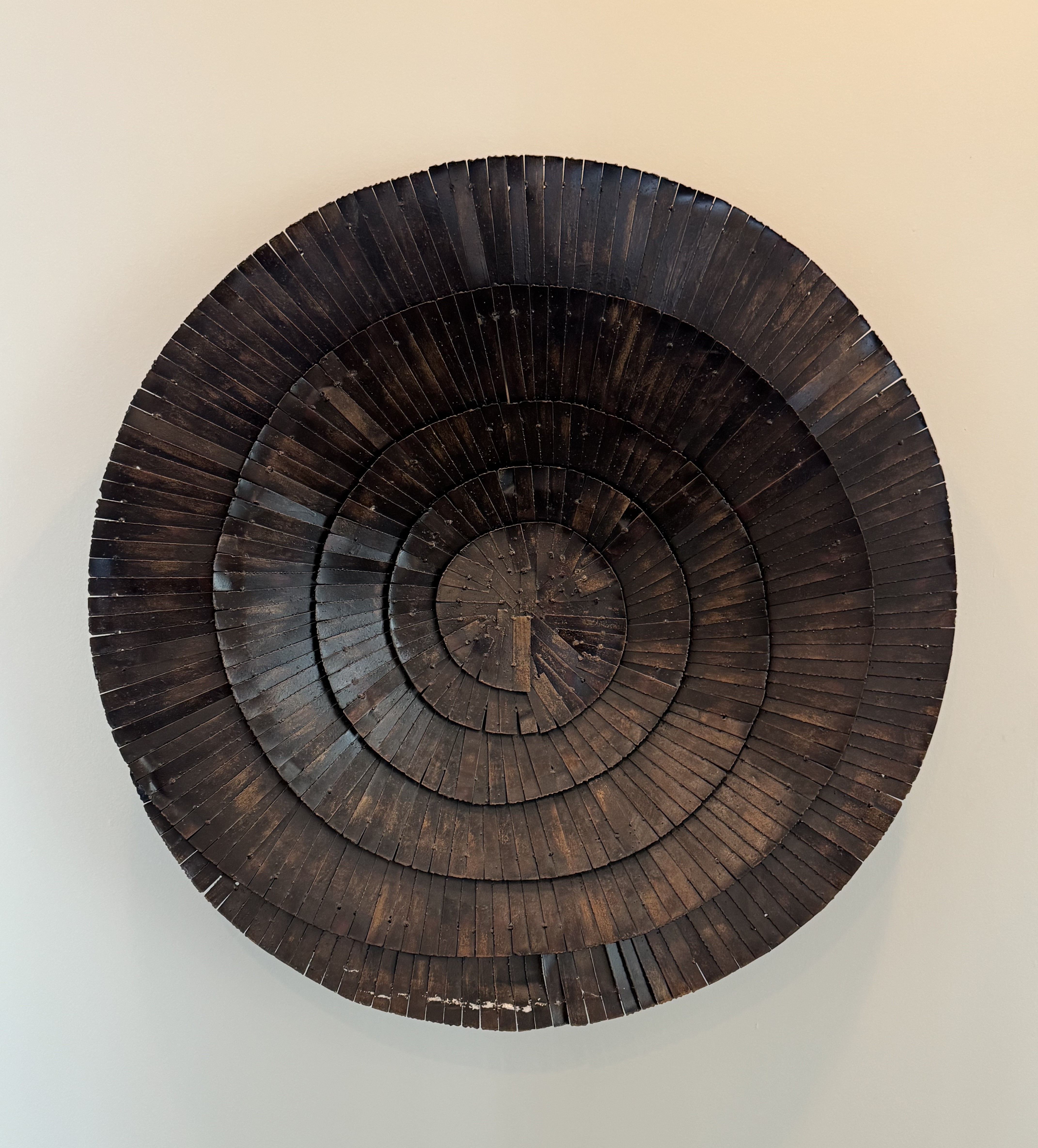 Close-up of a dark wooden circular art piece made of concentric rings with evenly spaced vertical segments.
