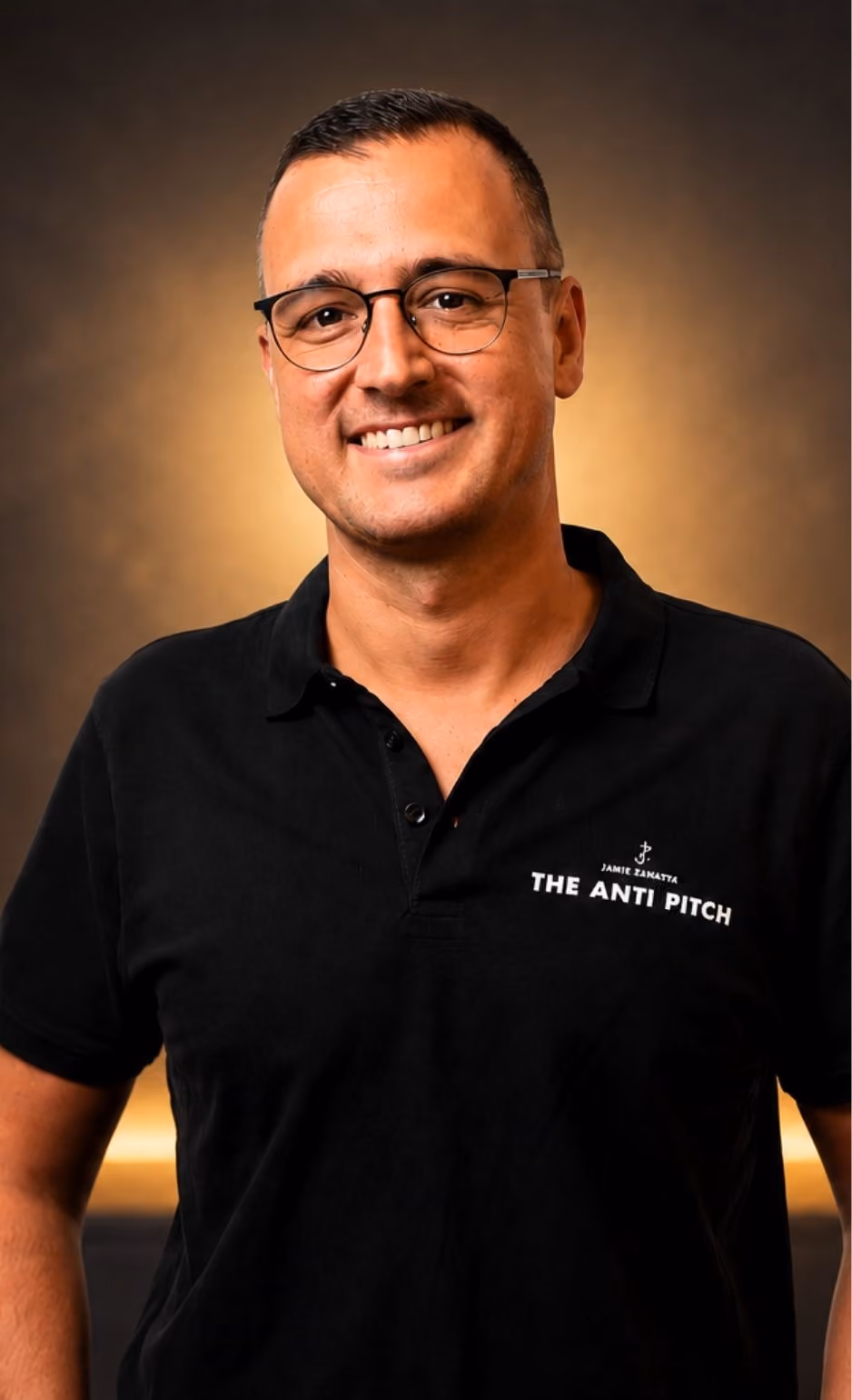Smiling man wearing glasses and black polo shirt with 'The Anti Pitch' text, glowing background.