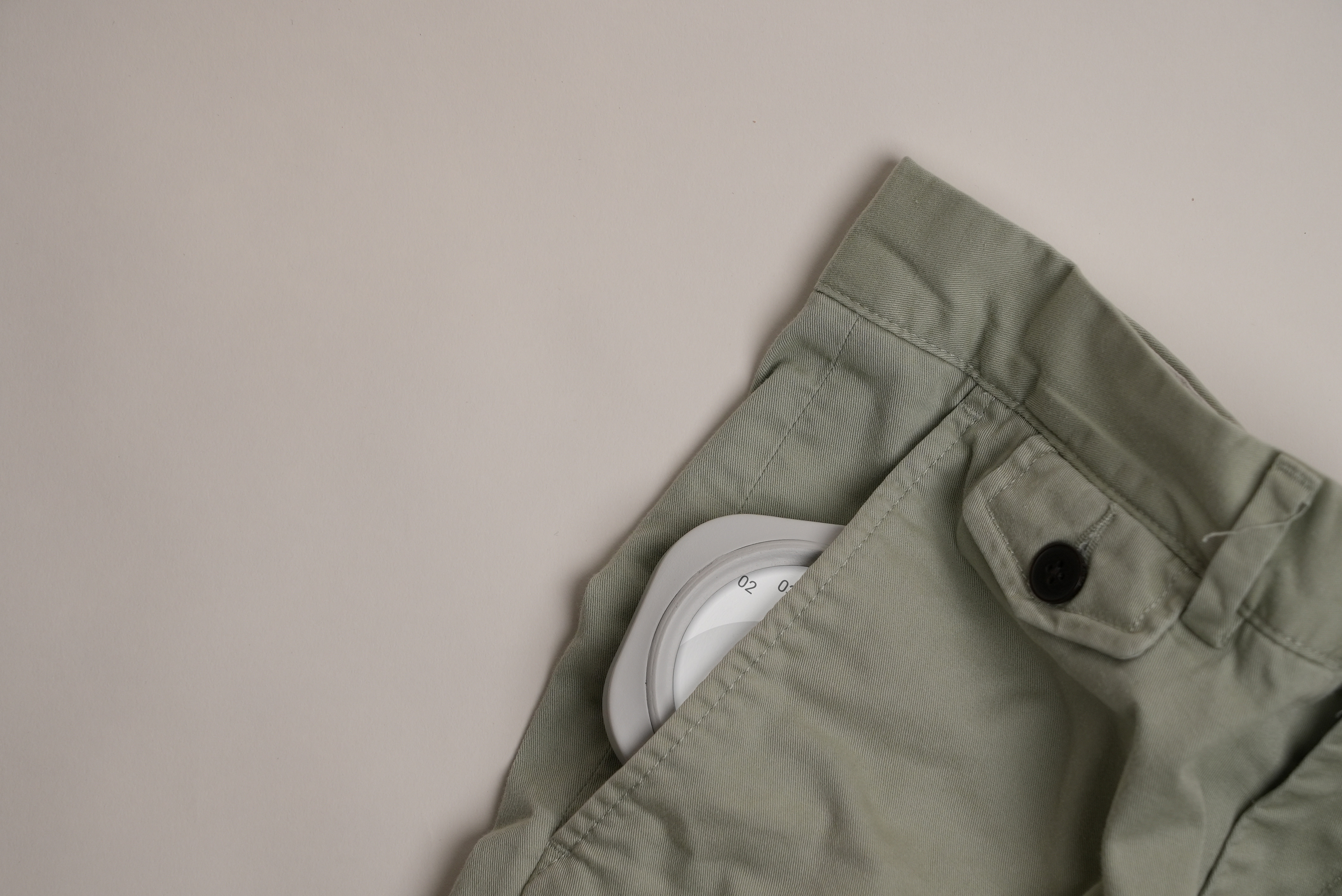 Top portion of light green pants with a white circular dial partially visible in the front pocket.