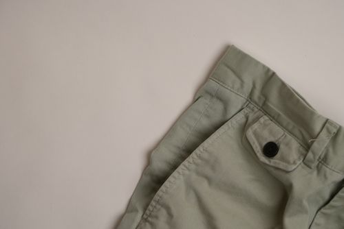 Close-up of the waistband and pocket area of light green pants with a black button on a beige background.